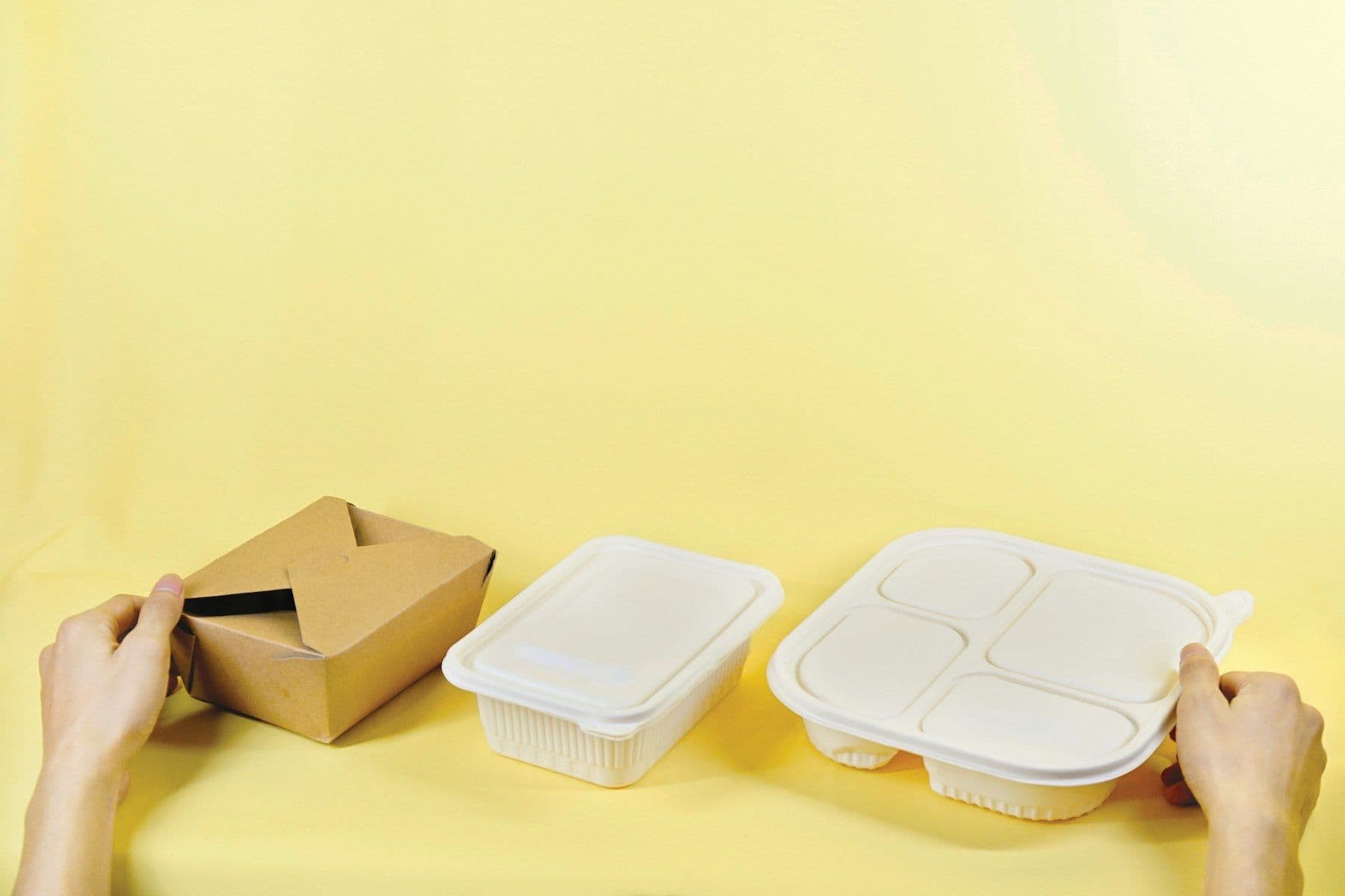 Hands holding a kraft takeaway box and plastic containers